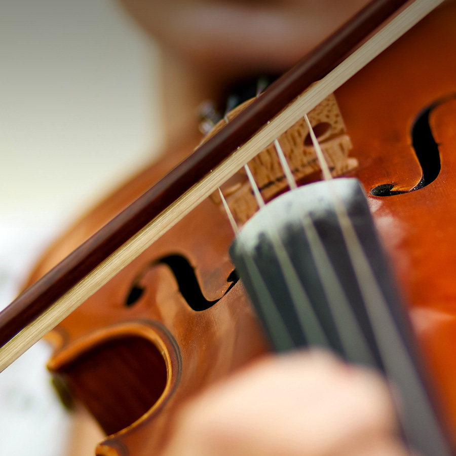 A close-up view of a wooden violin being played, showing the bow resting across the strings near the bridge and f-hole.